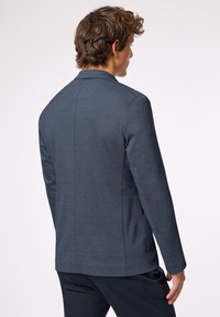 Granatowy żakiet o fakturze z dopasowanym krojem i długimi rękawami. Posiada subtelną pionową linię i pojedynczą wentylację z tyłu.