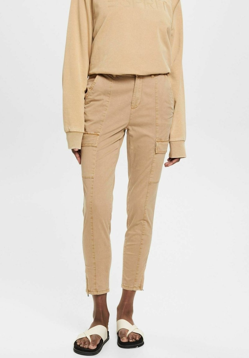 Beige cargobyxor med en figurnära design, som har fram- och bakfickor, dragkedjedetaljer vid anklarna och ett slätt bomullsmaterial.