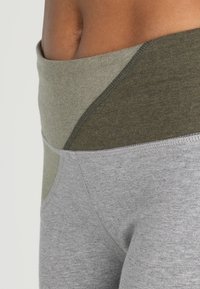 Leggings grigi e verde oliva con un design a blocchi di colore, dotati di una ampia vita elastica e di una morbida e elastica texture del tessuto.