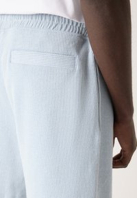 Light blue ribbed joggers feature an elastic waistband and a back pocket. The fabric has a textured finish with vertical stripes.