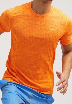 Man rent in een feloranje Nike shirt met korte mouwen en blauwe sportshorts, bij de hals en midden van het been bijgesneden.