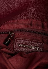 Wnętrze burgundowej torebki skórzanej z zamykaną na zamek kieszenią, fakturowaną tkaniną i srebrną etykietą "wonders". Widoczne gładkie detale haftu.