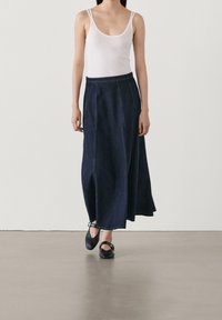 Mörkblå denim maxikjol, med en figursydd midja, flödande silhuett och vertikala sömmar. Buren med en vit linne och svarta ballerinas.