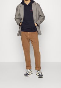 Grau gestreifter Over-Sized-Blazer über einem navy Hoodie, kombiniert mit beigen Chinos und mehrfarbigen Sneakers mit auffälligen Sohlen.