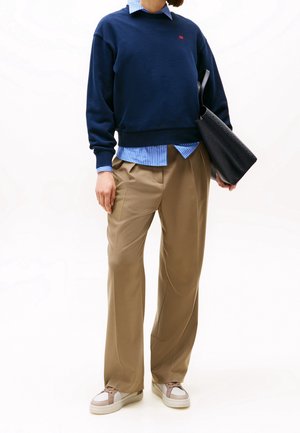 Merimerkki collegepaita punaisella logolla, päällä vaaleansininen raidallinen paita. Beiget housut ja harmaat lenkkarit, joissa on valkoisia ja ruskeita yksityiskohtia.