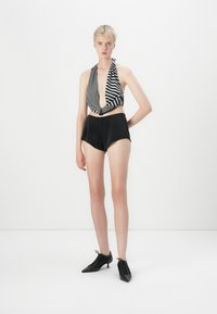 Zwart-wit gestreepte haltertop met een diepe halslijn, gecombineerd met hoge zwarte shorts en zwarte veterschoenen.