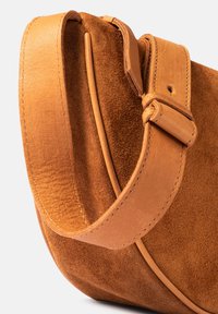 Brown suede handbag with smooth leather strap, detailed stitching, and a curved, structured shape. Strap features a buckle closure.