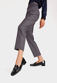 Pantaloni grigi su misura con una leggera affusolatura, abbinati a mocassini neri lucidi con un accento dorato. Texture liscia e design elegante.