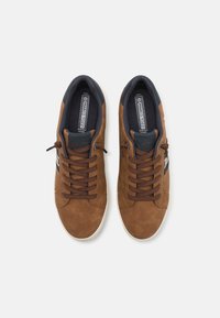 Baskets en daim marron avec des lacets marron, une doublure bleu marine et une semelle en caoutchouc. Elles présentent un logo sur le côté et une finition texturée.