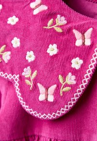 Rosa Cord-Stoff mit bestickten Blumen- und Schmetterlingsmotiven, ausgestattet mit einem gewellten Kragen und dekorativen weißen Nähten.