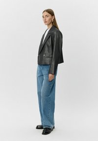 Zwarte metallic blazer met een iets cropped ontwerp, dubbele knopen en gestructureerde schouders, gecombineerd met lichtblauwe straight-leg jeans.