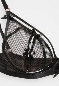 Sort mesh-bh med glansfulde detaljer, der har en trekantet form, bånddetaljer og en struktureret design. Bløde stropper og justerbar hardware inkluderet.