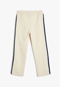 Cremefarbene Hosen mit weicher Textur, die Navy-Seitestreifen, einen elastischen Bund und ein gerades Bein Design aufweisen.