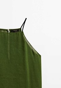 Zielona lniana bluzka z cienkimi czarnymi ramiączkami, z zapięciem na guziki z tyłu oraz luźnym, minimalistycznym krojem. Miękka tekstura, casualowy styl.