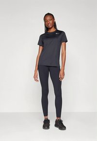 Černé atletické tričko s krátkými rukávy a kulatým výstřihem v kombinaci s černými legínami. Na hrudi je malé logo Nike.