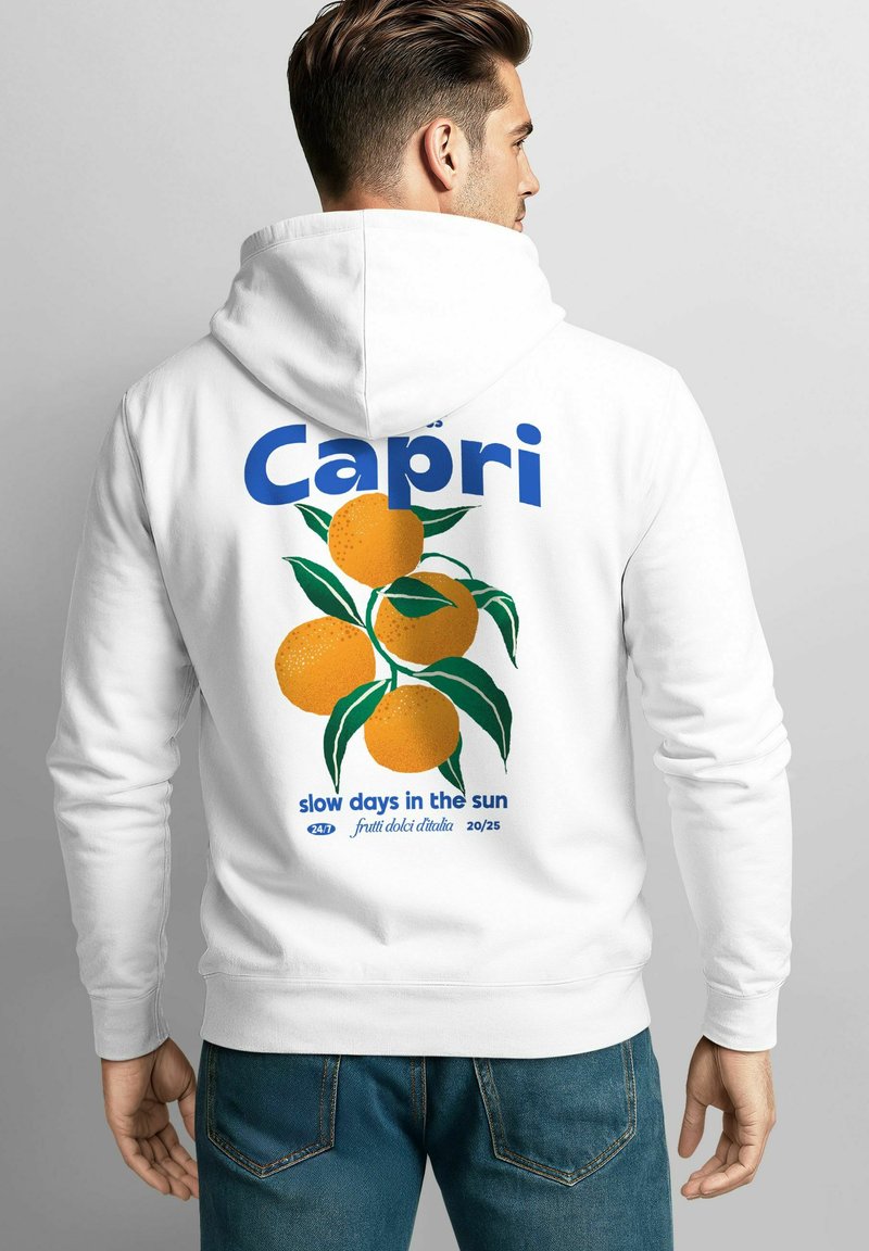 Mann trägt einen weißen Hoodie mit blauer "Capri"-Beschriftung und einer Illustration von Orangen mit grünen Blättern auf dem Rücken, kombiniert mit blauen Jeans.