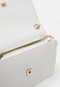 Vit läderhandväska med guldhardware, som har en magnetisk knäppning och ett fack med dragkedja för säker förvaring.