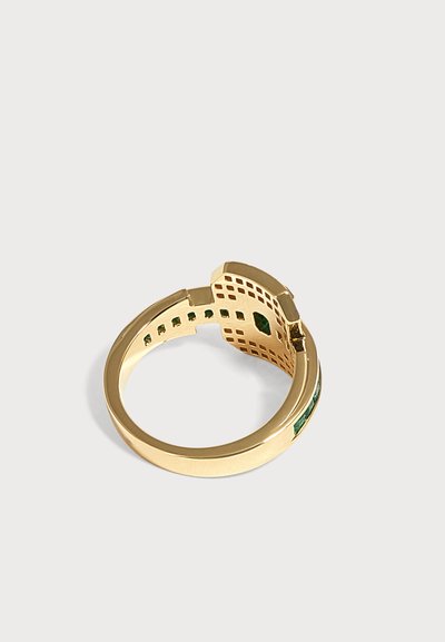 Bague en or avec un motif à grille et de petites pierres vertes serties à l'intérieur de l'anneau, présentée sur un fond clair uni.