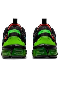 Paire de baskets noires avec talons verts vifs, semelles translucides vertes et doublures intérieures rouges, vues de dos sur fond blanc.