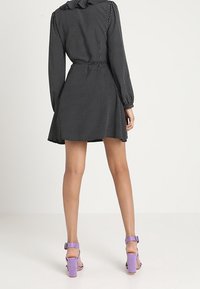 Schwarz gepunktetes Kleid mit tailliertem Schnitt, langen Ärmeln und schwingendem Rock. Kombiniert mit lavendelfarbenen Blockabsatzsandalen.
