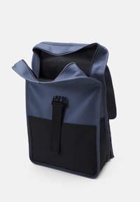 Plavi i crni ruksak napravljen od glatkog, vodootpornog materijala. Ima otvoreni vrh, podesivu traku i posebnu donju džepu.