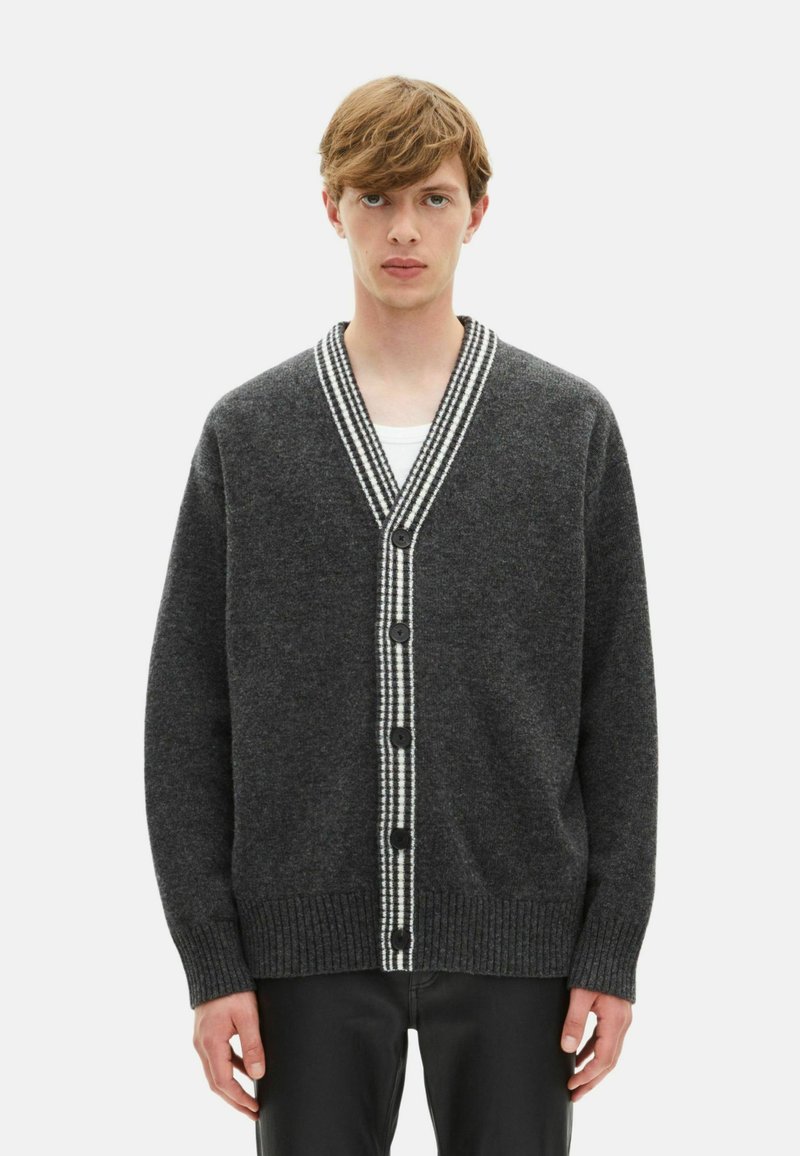 Donkergrijze wollen cardigan met een V-hals, witte gestreepte rand, zes zwarte knopen en geribbelde manchetten en zoom. Zachte textuur, relaxed fit.