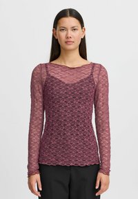 Spitzenbluse mit langen Ärmeln in tiefem Mauve, die mit einem floralen Muster, einem gewellten Saum und einem geschichteten Design ausgestattet ist, das eine Unterlage freilegt.