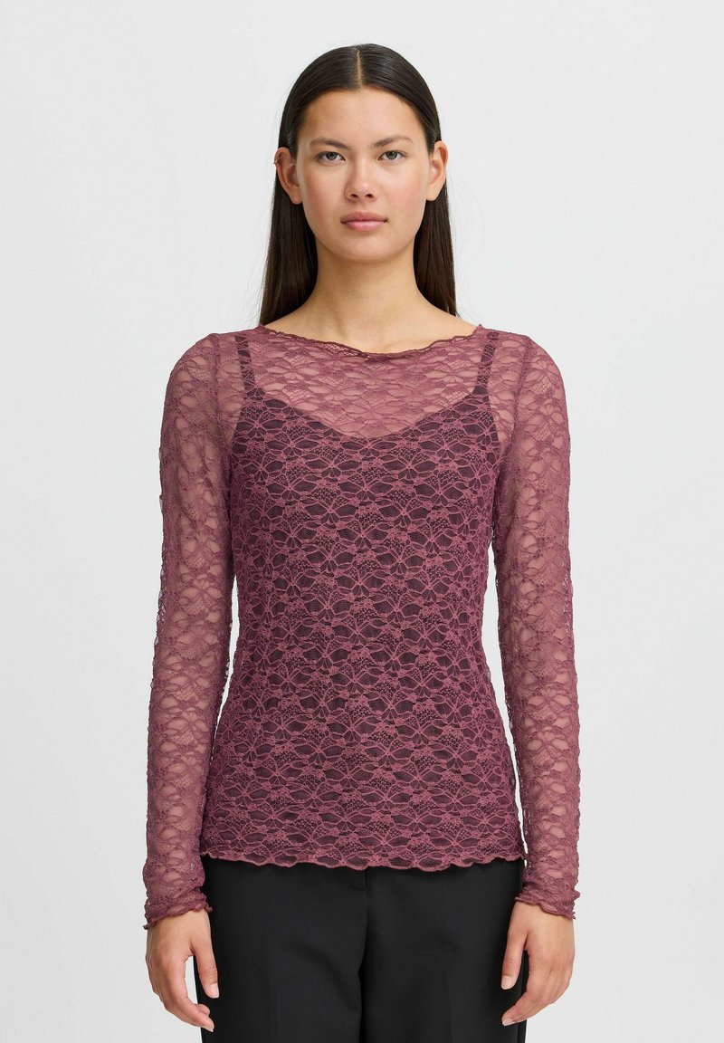 Spitzenbluse mit langen Ärmeln in tiefem Mauve, die mit einem floralen Muster, einem gewellten Saum und einem geschichteten Design ausgestattet ist, das eine Unterlage freilegt.