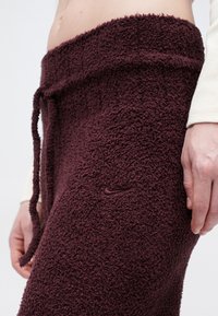 Bordové, chundelaté tepláky s mäkkou textúrou, elastickým pásom a nastaviteľnou šnúrkou. Malé hnedej Nike logo na boku.