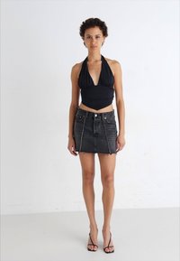 Svart halterneck-top med dyp V-hals og rynket design, kombinert med en tettsittende svart denim mini-skjørt med glidelås foran, synlige sømmer og frynset kant.
