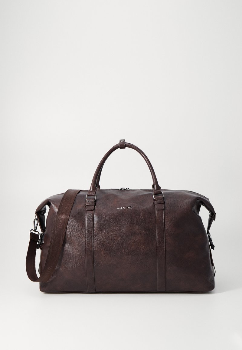 Mala de viagem em couro castanho com alças duplas, tira de ombro destacável e branding mínimo. Textura suave com variações subtis.