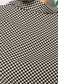 Černobílá kostkovaná tkanina s vlnitou texturou, která obsahuje vzor malých čtverců vytvářející zkreslený vizuální efekt.