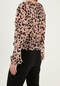 Blusa con stampa leopardata rosa e nera, dotata di cappuccio, maniche lunghe, polsini arricciati e orlo a volant. Materiale leggero e trasparente.