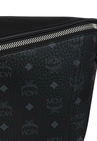 Close-up van zwart gestructureerd leren tasgedeelte met zilveren ritssluiting en herhaald MCM-logo en diamantpatroon.