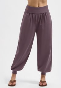 Lässig sitzende, pflaumenfarbene Hose mit gerafftem Bund und Säumen, getragen mit braunen Sandalen, vom Bund bis zu den Füßen auf weißem Hintergrund dargestellt.