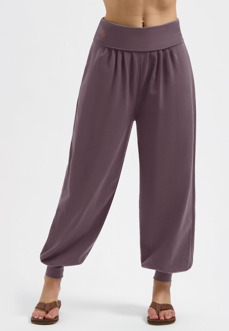 Lässig sitzende, pflaumenfarbene Hose mit gerafftem Bund und Säumen, getragen mit braunen Sandalen, vom Bund bis zu den Füßen auf weißem Hintergrund dargestellt.