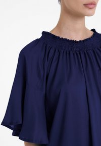 Top blu navy con scollo arricciato, maniche corte a campana e un tessuto morbido al tatto, che mette in risalto un design rilassato.