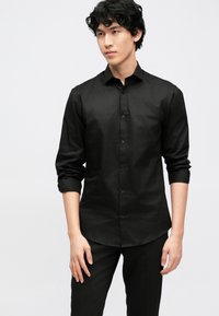 Zwarte overhemd met knopen, gemaakt van gladde stof, voorzien van lange mouwen, een klassieke kraag en een afgeronde zoom. Draagt bijpassende zwarte broek.