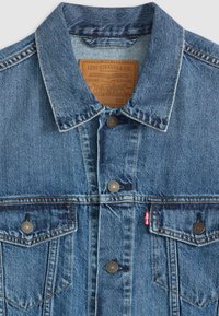 Chaqueta de mezclilla en azul claro, con cierre de botones en la parte delantera, cuello puntiagudo, costuras decorativas y dos bolsillos en el pecho con botones de metal.