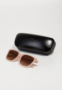 Óculos de sol em acrílico rosa com lentes castanhas, armação geométrica e detalhes em tom dourado. Acompanhados de um estojo rígido preto com logótipo em relevo.