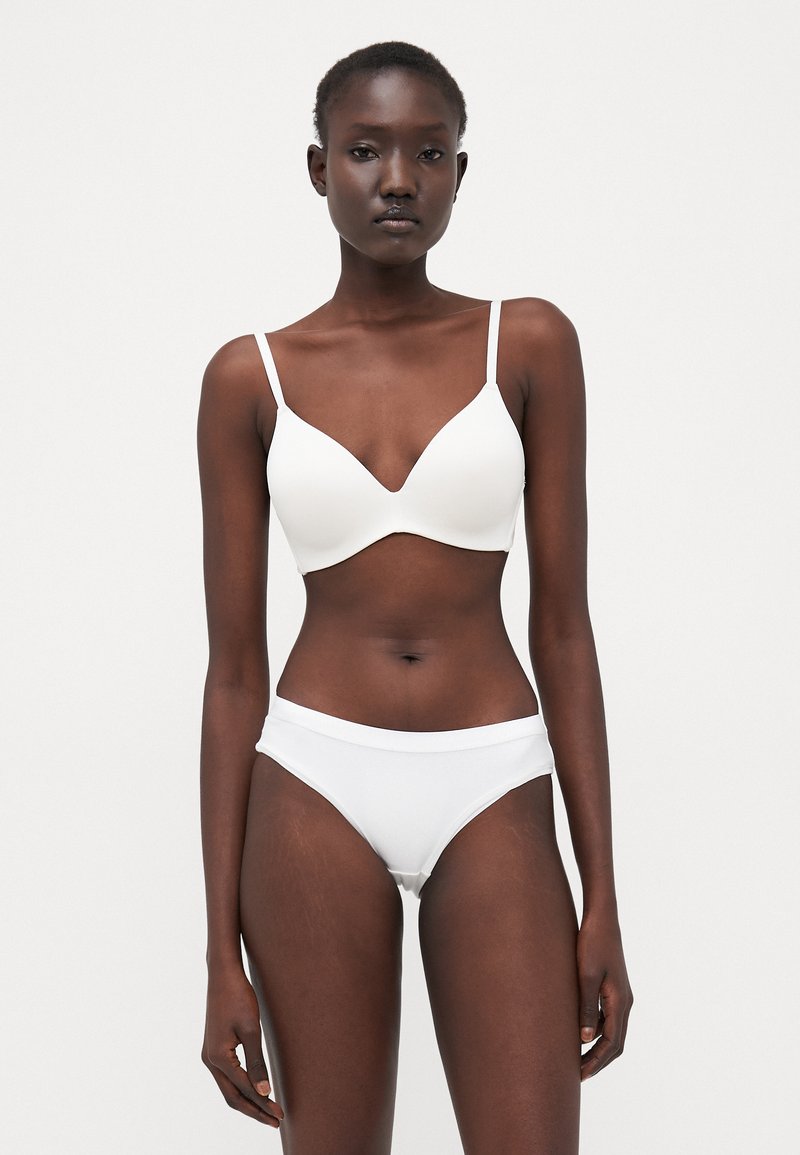 Vit bh med justerbara axelremmar och design med djup V-ringning tillsammans med matchande bikinitrosor med hög midja. Mjukt, slätt tyg, minimal sömnad.