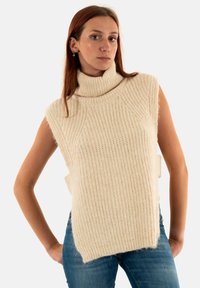 Suéter sin mangas de punto en color beige claro, que presenta un patrón texturizado y aberturas laterales. Tejido suave con un corte relajado.