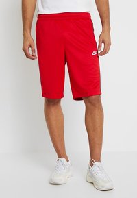 Red athletic shorts made of lightweight fabric with an elastic waistband, featuring a small white Nike logo on the left leg.