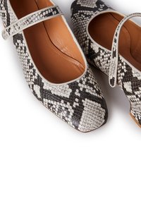 Zapatos planos con punta redonda y una tira estrecha en el empeine. La paleta de colores incluye tonos negros, blancos y beige.