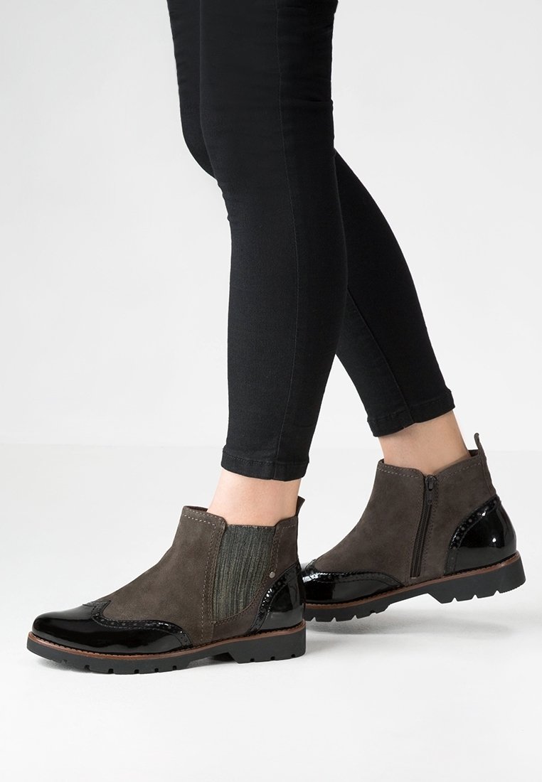 Bottes noires et gris foncé montant à la cheville, avec fermeture éclair latérale et panneau élastique, portées avec un pantalon skinny noir.