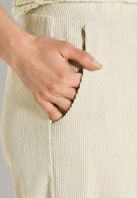 Hand rustend in de zijzak van beige ribgebroken corduroybroek.