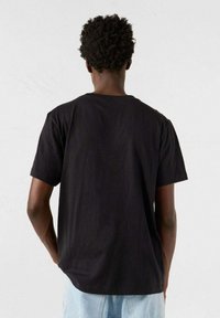 T-shirt in cotone nero con vestibilità rilassata, maniche corte e scollo a giro, mostrato dal retro su uno sfondo neutro.