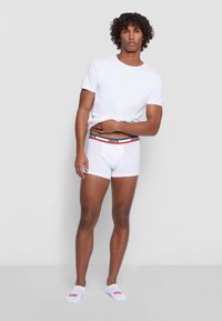 White t-shirt and white boxer briefs with a red and black Levi's waistband. Model wearing white ankle socks with red logo.