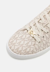 Beige patterned sneaker with a smooth texture, featuring a white rubber sole and gold logo accent on the lace eyelet.