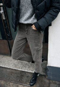 Szare spodnie cargo z bocznymi kieszeniami, zestawione z teksturowanym szarym swetrem i czarną puchową kurtką. Stylizację dopełniają czarne botki za kostkę.